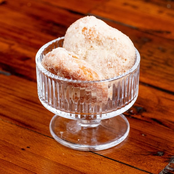 Two sugar-dusted pastries in a clear glass dessert dish on a rustic wooden table.