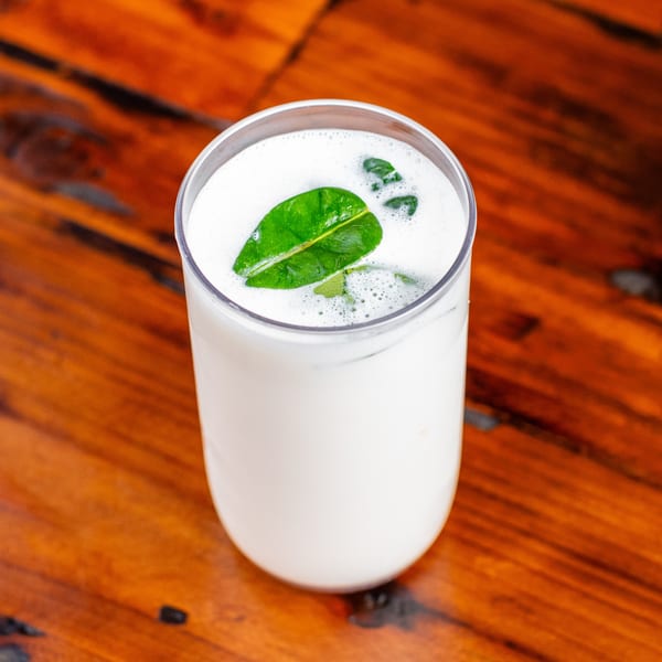 A tall glass of white frothy drink, garnished with green leaves, on a wooden table.