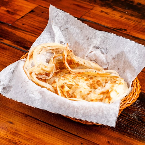 Golden-brown roti bread, torn into pieces, served in a wicker basket lined with white paper.