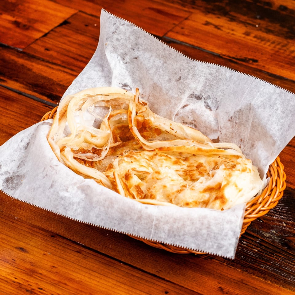 Golden-brown roti bread, torn into pieces, served in a wicker basket lined with white paper.