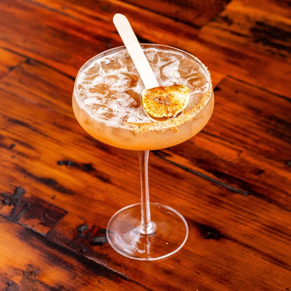 Iced cocktail with a sugared rim, garnished with a lime wedge and a wooden stirrer on a wooden table.
