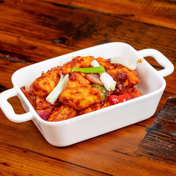 Spicy paneer chili with red and green bell peppers, onions, and scallions in a white dish.