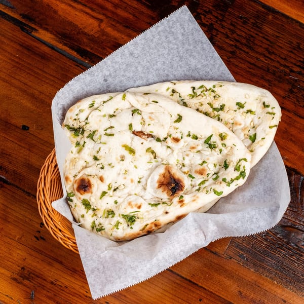 Two pieces of garlic naan bread with cilantro in a basket on a wooden table.