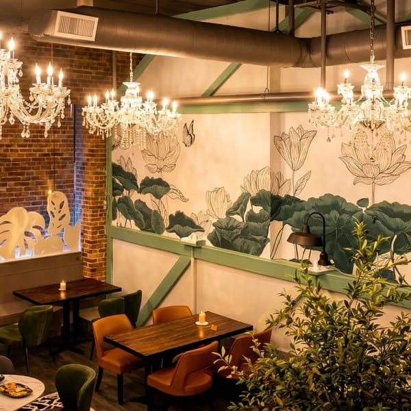 Restaurant interior with crystal chandeliers, brick walls, and a mural of lotus flowers and leaves.