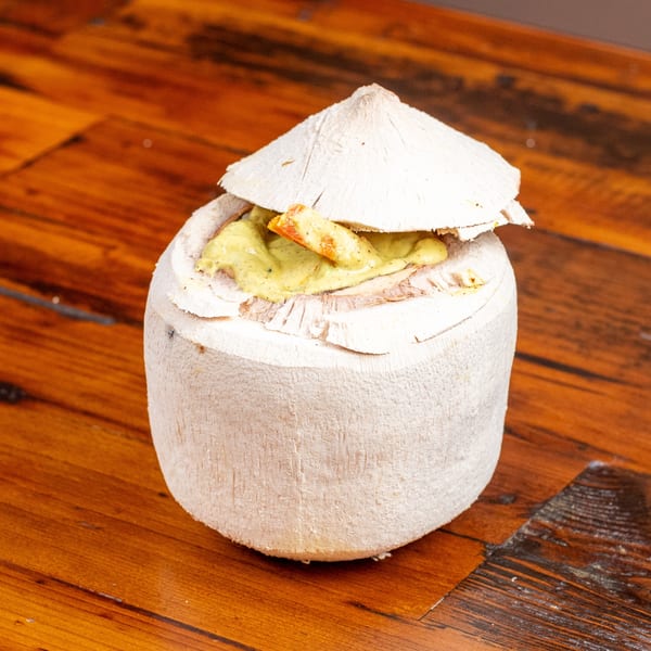 Coconut shell filled with a creamy green sauce and shrimp, on a wooden table.