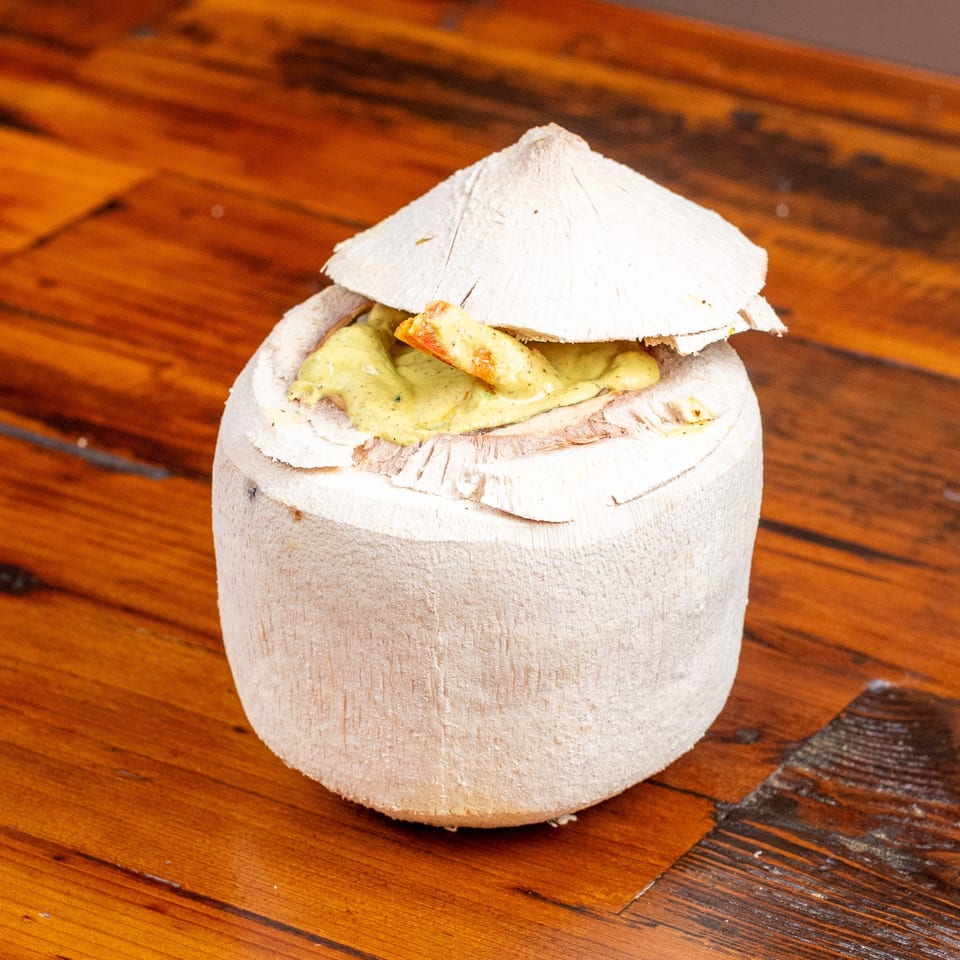 Coconut shell filled with a creamy green sauce and shrimp, on a wooden table.