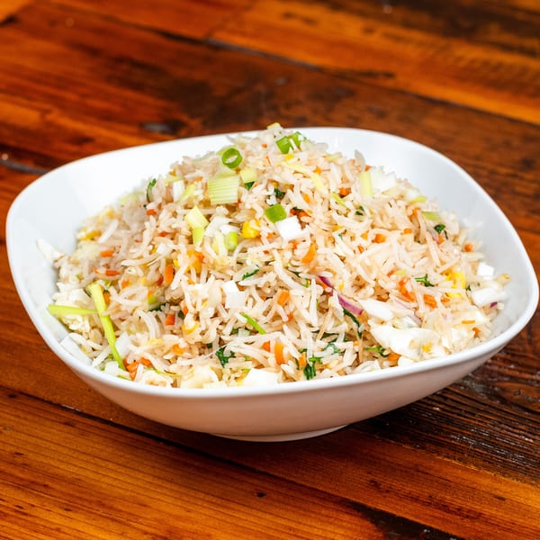 A white bowl filled with vegetable fried rice, garnished with chopped green onions, on a wooden table.