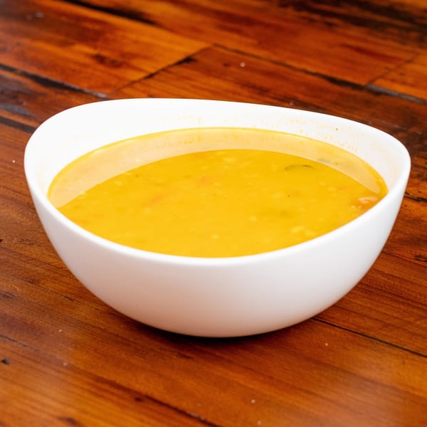 A white bowl filled with vibrant yellow soup sits on a rustic wooden table.