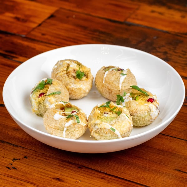 Six pani puri, filled with avocado, pomegranate, and cilantro, drizzled with white sauce.
