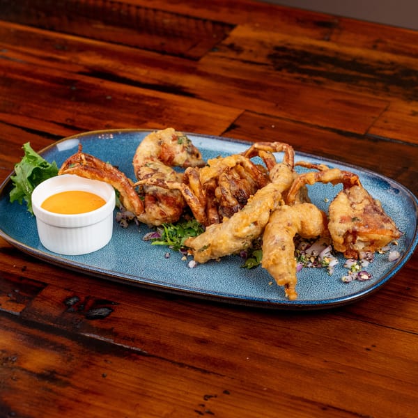 Crispy fried soft-shell crabs on a blue plate with lettuce, chopped herbs, and a side of orange sauce.