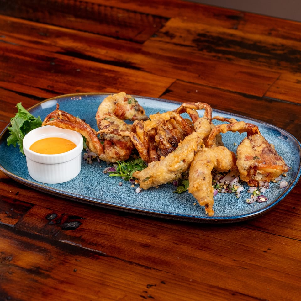 Crispy fried soft-shell crabs on a blue plate with lettuce, chopped herbs, and a side of orange sauce.