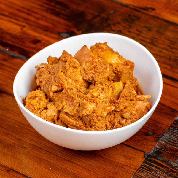 A white bowl filled with chunky, orange-brown stewed meat sits on a dark wooden table.